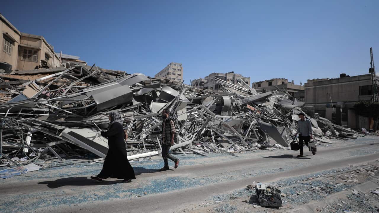 Three people walking past the rubble of a destroyed building.