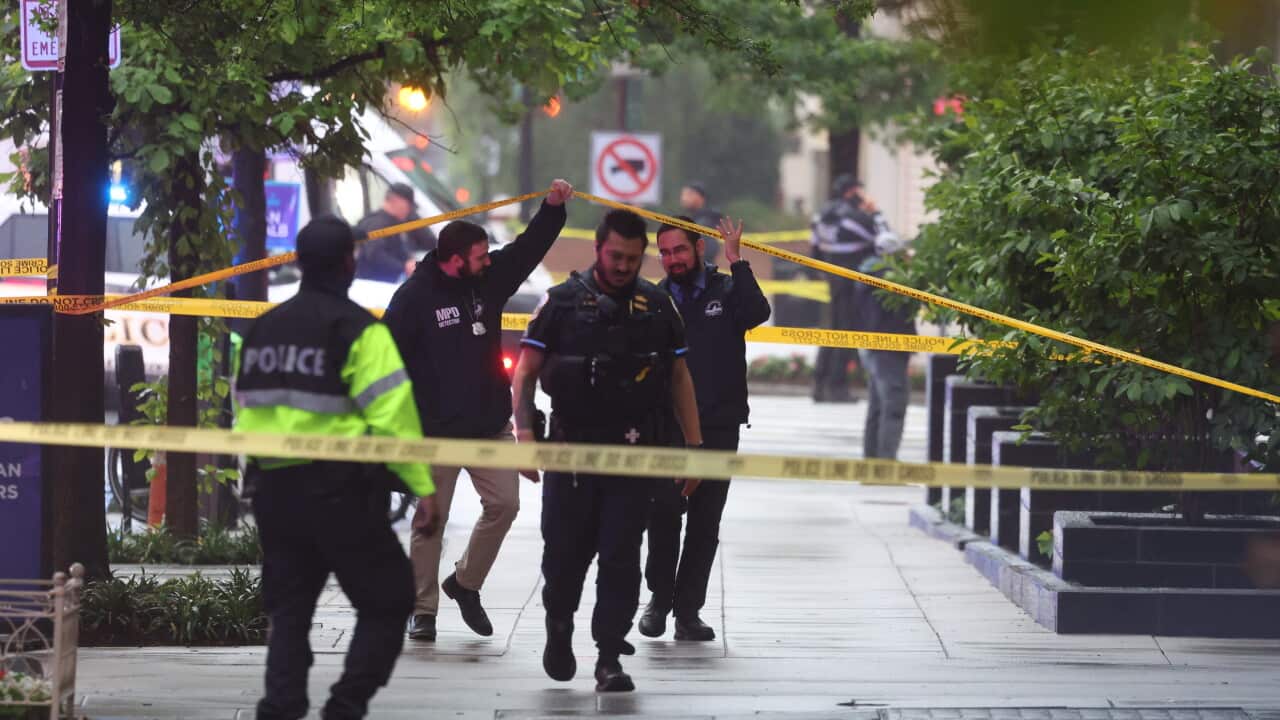 Police holding up tape as they inspect the scene of a shooting on a street