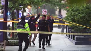 Police holding up tape as they inspect the scene of a shooting on a street