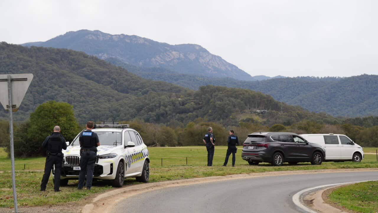 Police standing near vehicles at a large grassy area.