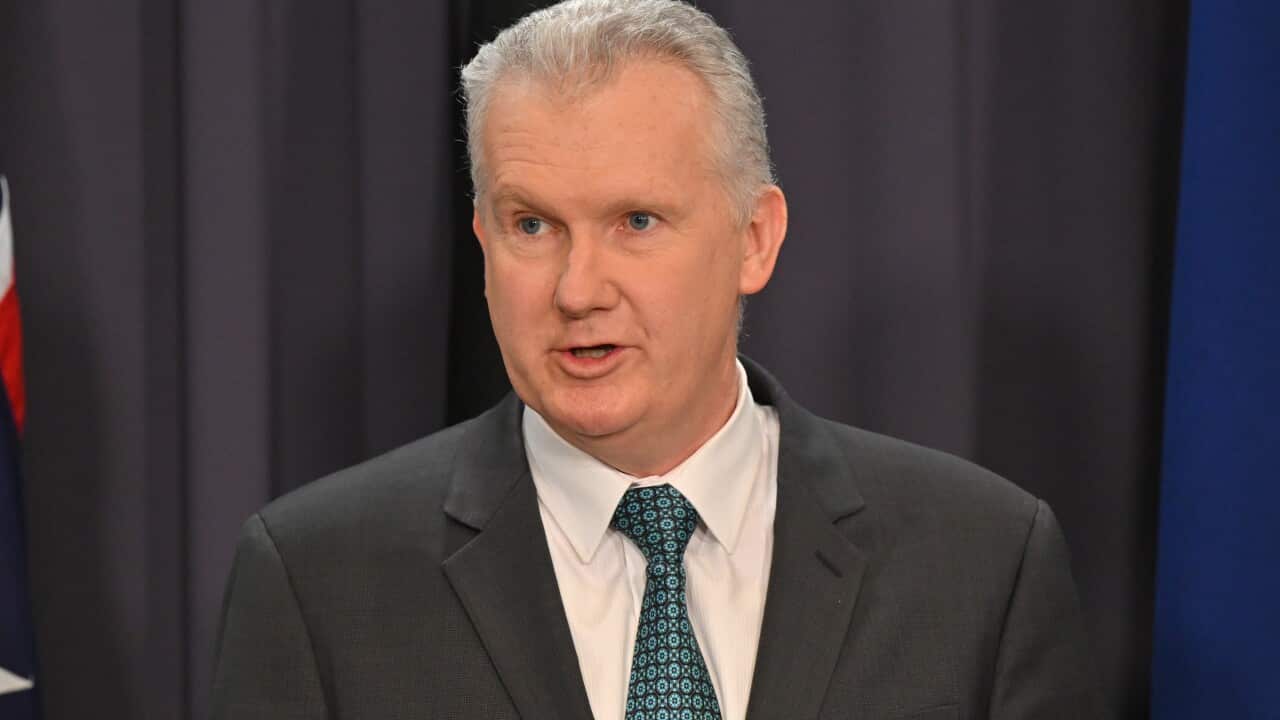 A man wearing a suit and tie speaking to journalists.