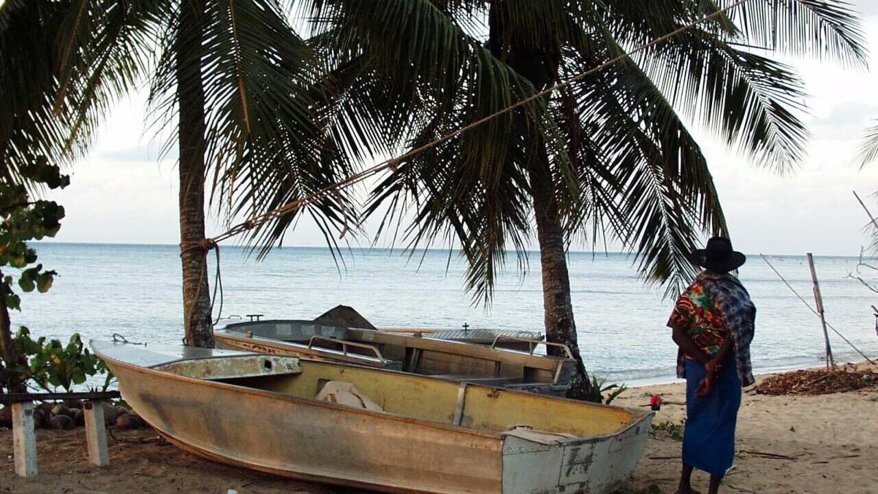 A man standing on the shore next to a small boat.