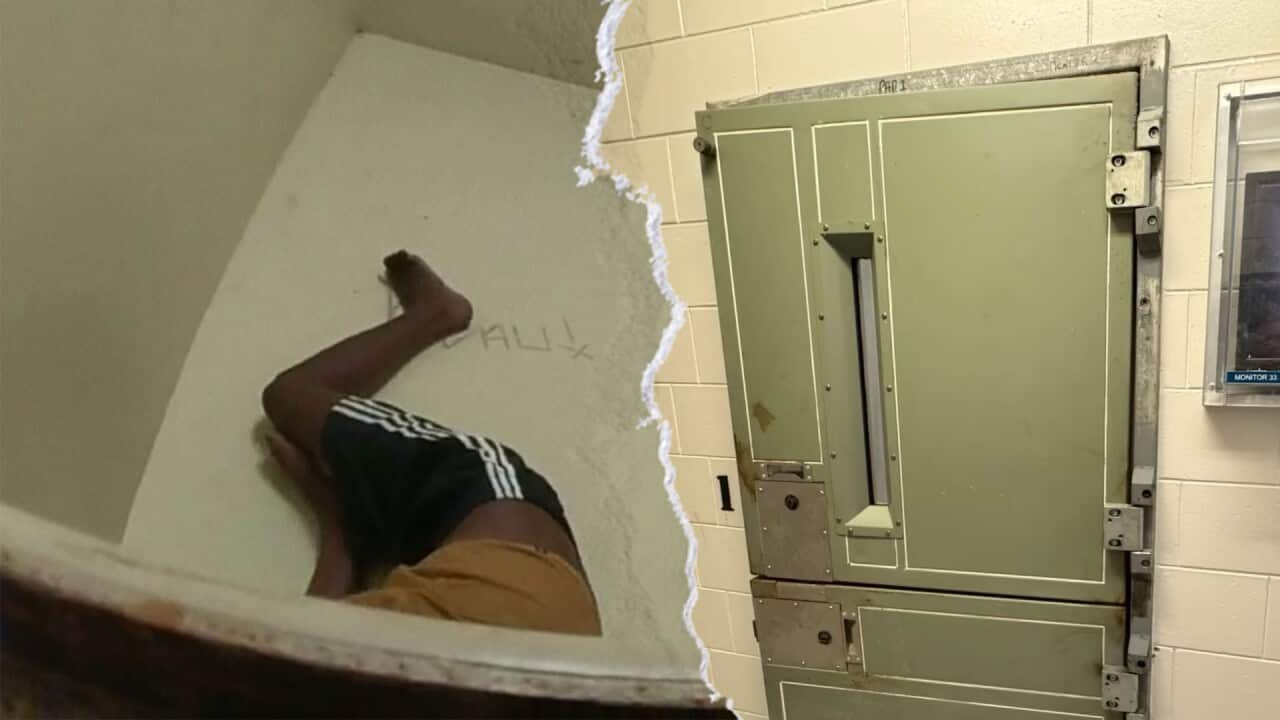 On the left, the legs of a teenage boy are sprawled on the floor of a tiny cell. On the right is the closed metal door of an isolation cell.