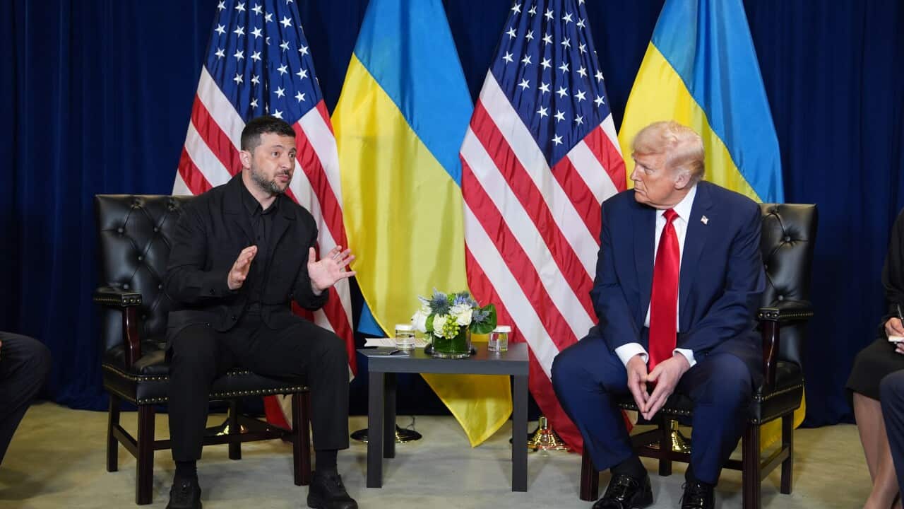 Volodymyr Zelenskyy speaks as he sits next to Donald Trump on a stage in front of the flags of the US and Ukraine.