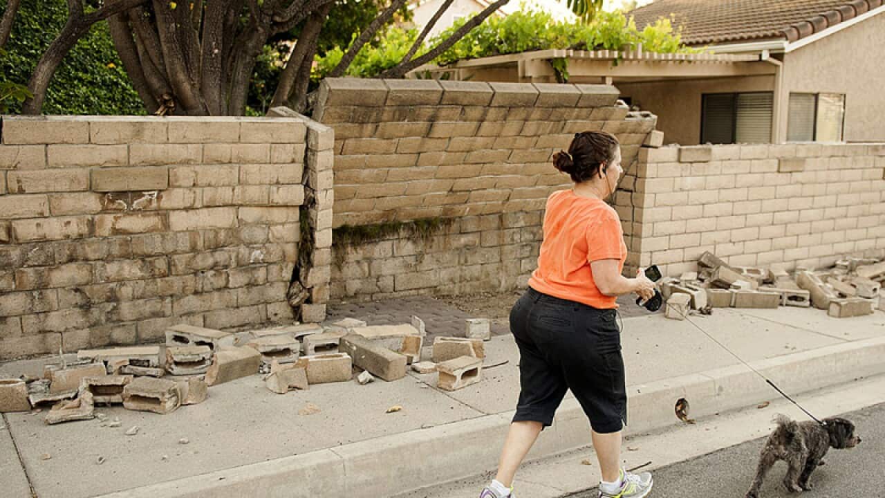 A woman walks her dog past a broken block wall in Fullerton, Calif.