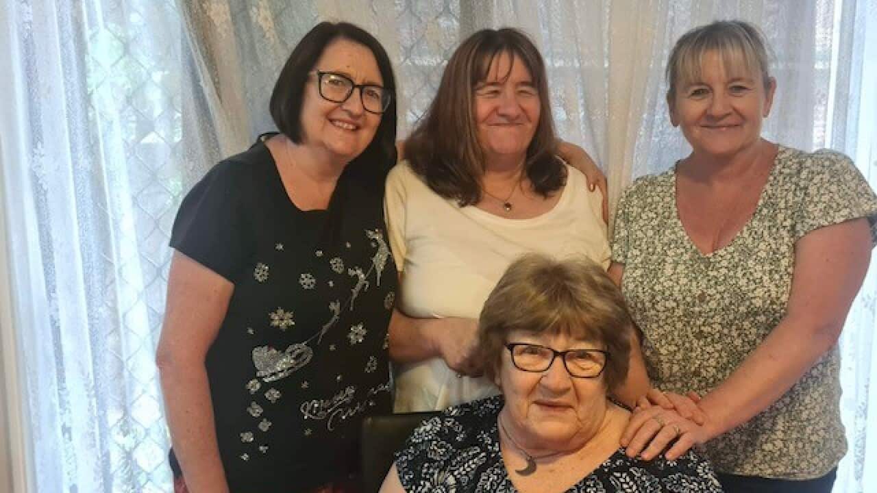 Three women are seen smiling in a photo with an older woman, who is their mother.