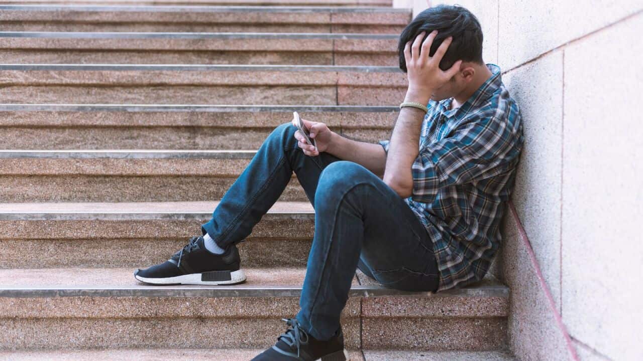 A young man looks at his mobile sitting on steps.