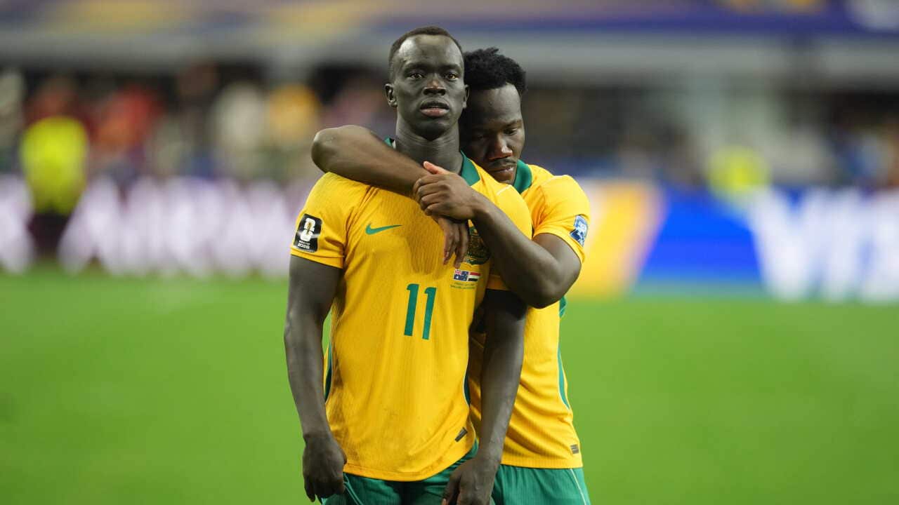 Two men in yellow and green jerseys sadly hug