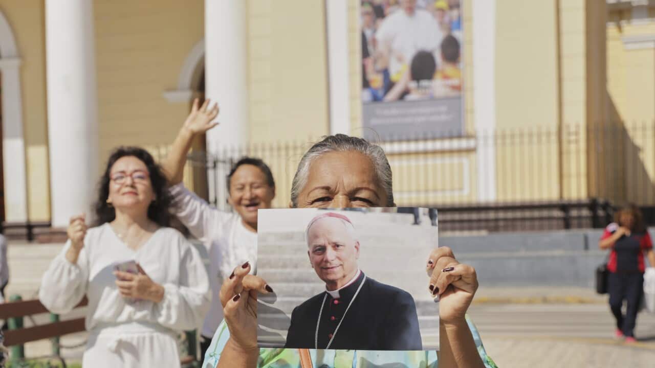 A woman holds a photo of Bishop Robert Prevost as two women behind her stand with jubilant expressions.