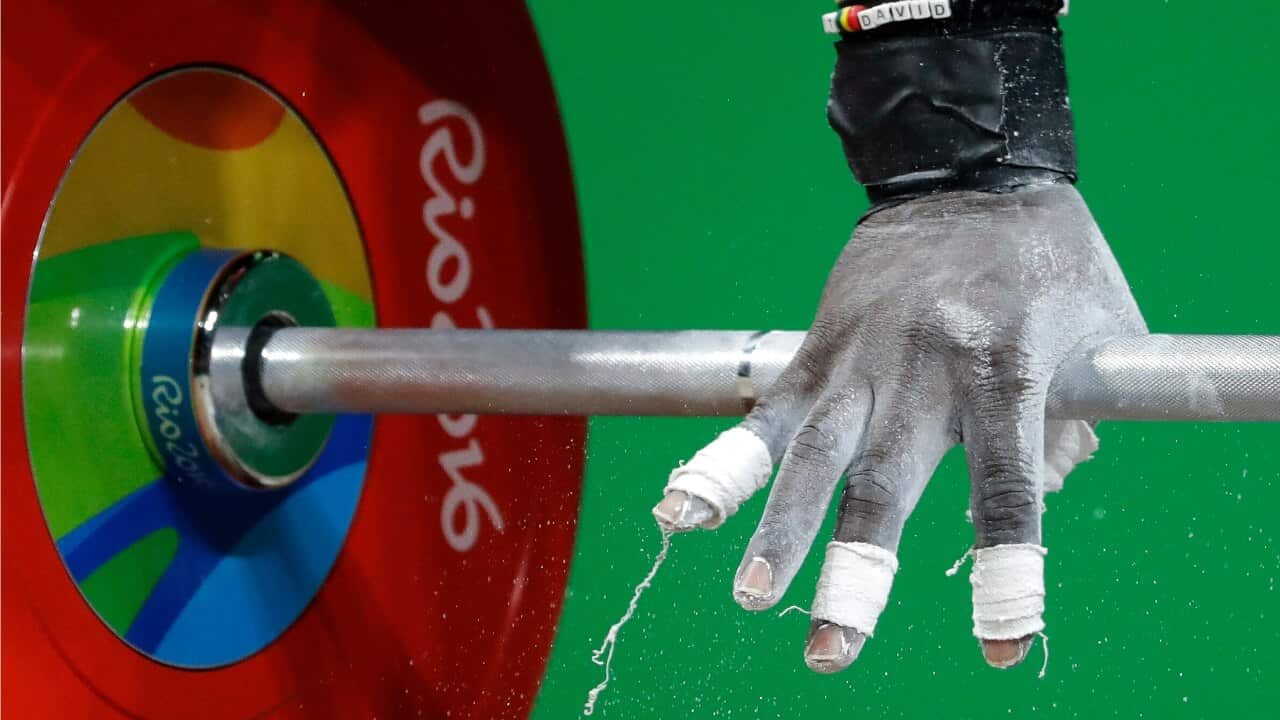 Petit David Minkoumba, of Cameroon, gets a grip on the barbell during the men's 94kg weightlifting competition.