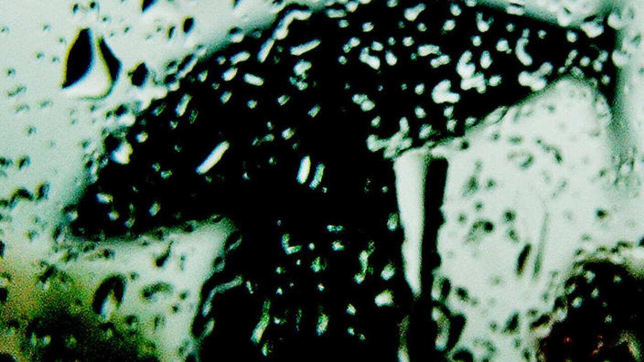 A man with an umbrella passes a rain-covered window in Freehold, N.J., Monday, May 3, 2004. (AP Photo/Daniel Hulshizer)