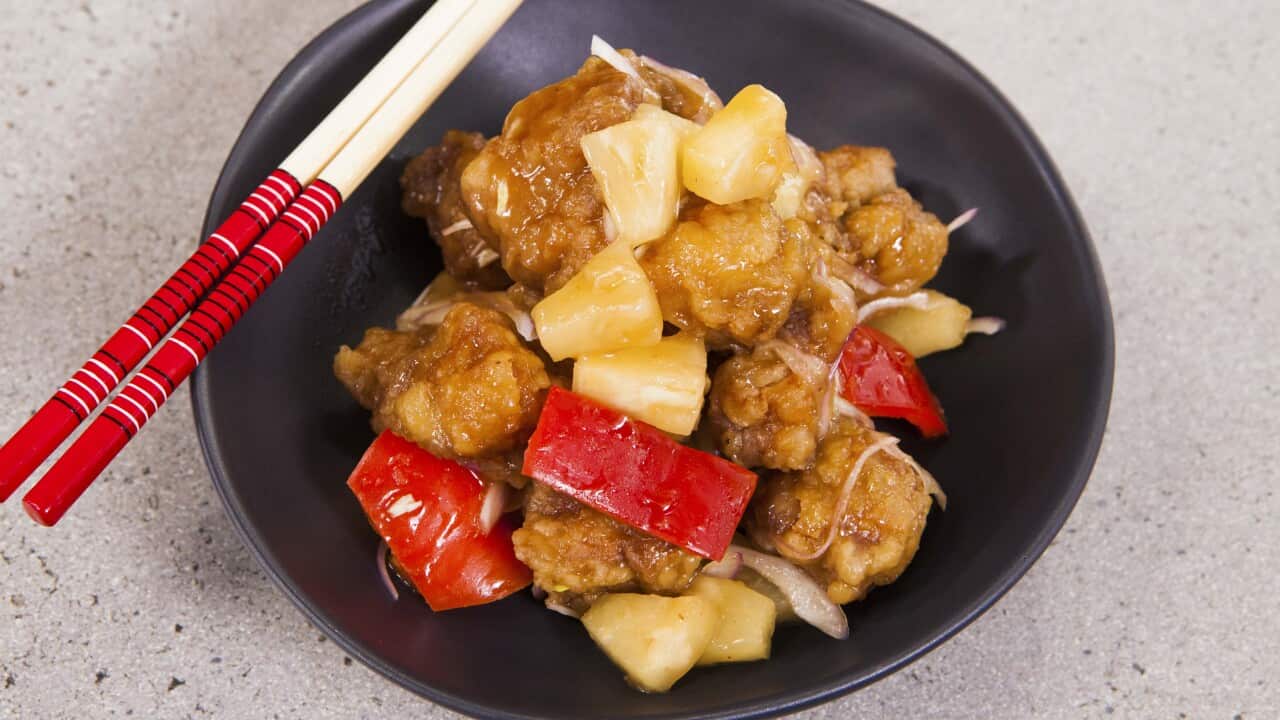 A serve of sweet and sour pork sits in a black bowl. Chopsticks rest on one edge.