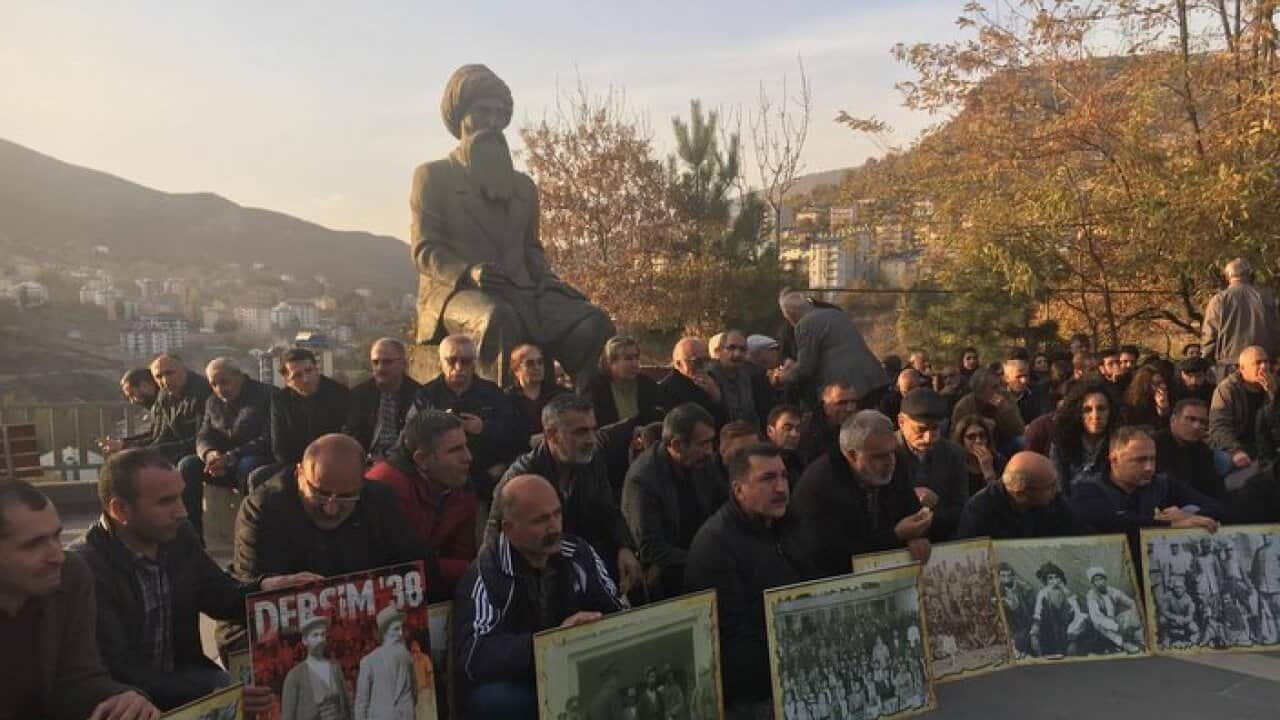 A group of people standing of Seyit Riza statue