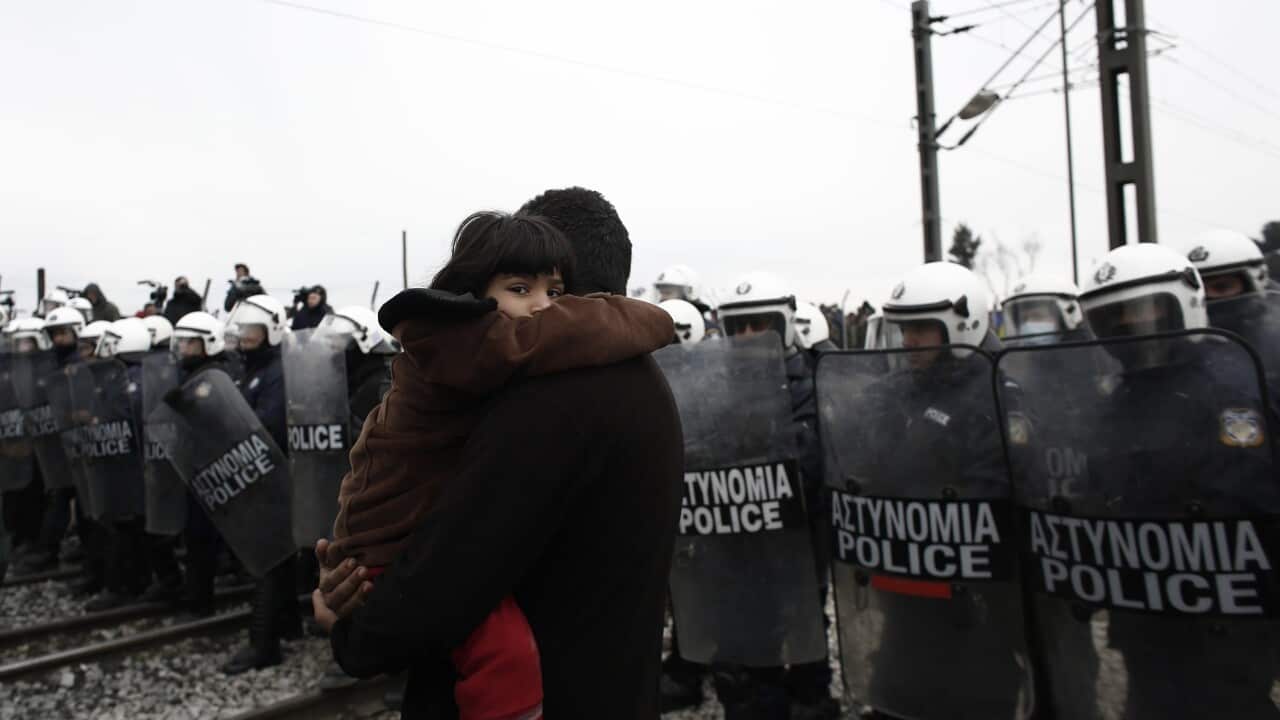 A Syrian refugee child looks as her father carry her in front of riot police during a protest