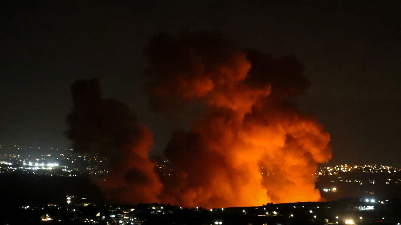 A cloud of red and orange smoke rises above a city skyline.