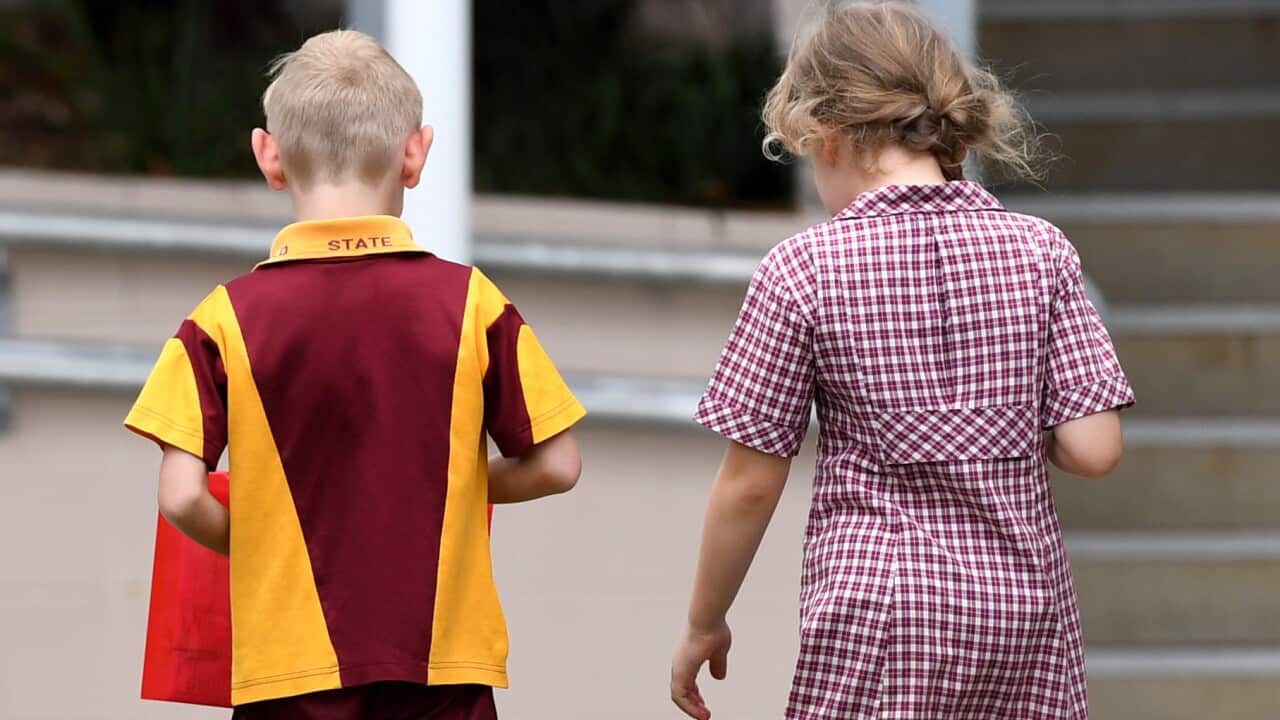 A boy in a maroon and yellow school uniform and a girl in a red and white checked dress.