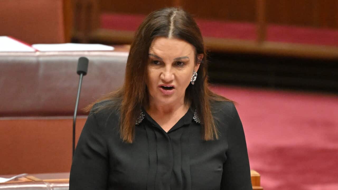A woman in a black top is holding papers as she speaks into a microphone.