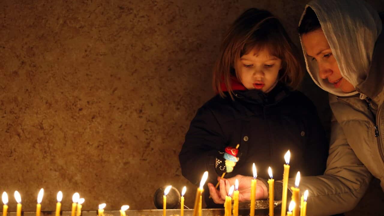 An Orthodox Serb woman and a child light candles in a cathedral.