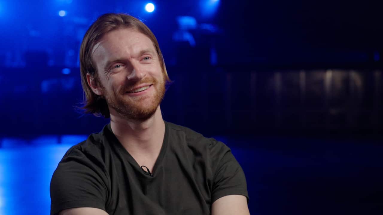 A man wearing a black t-shirt sitting and talking