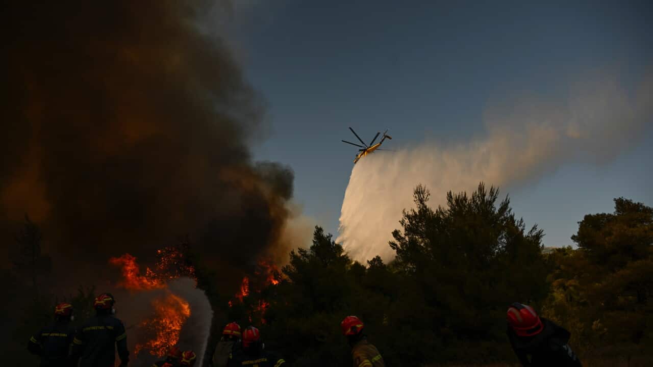 A firefighting helicopter drops water over a smoke-filled forest and fire in Greece.