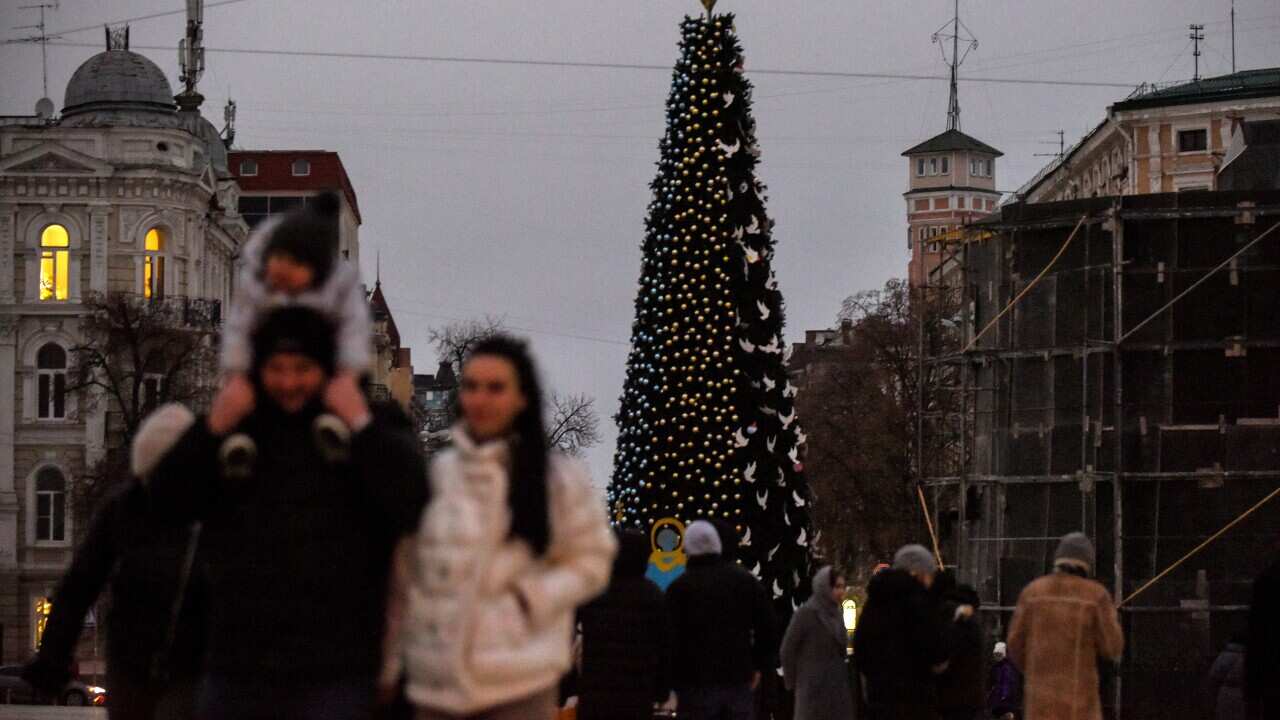 People walk by a Christmas tree installed at Sofiyska Square, in Kyiv, Ukraine, 18 December 2022.