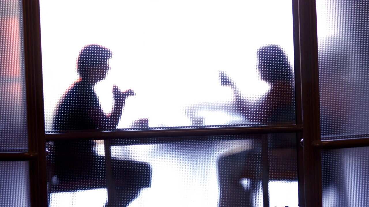 Two people's silhouettes behind a glass door. They're seated at a table talking.