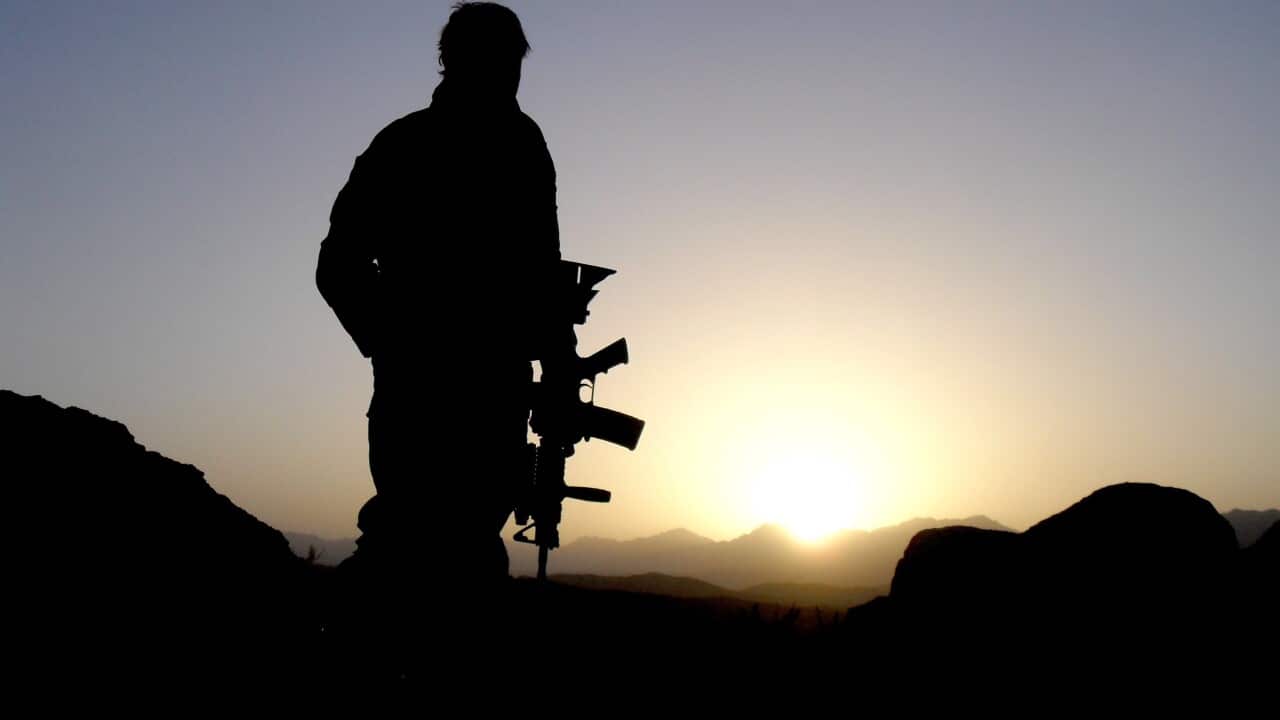 A silhouette of a soldier holding a gun standing on a mountain