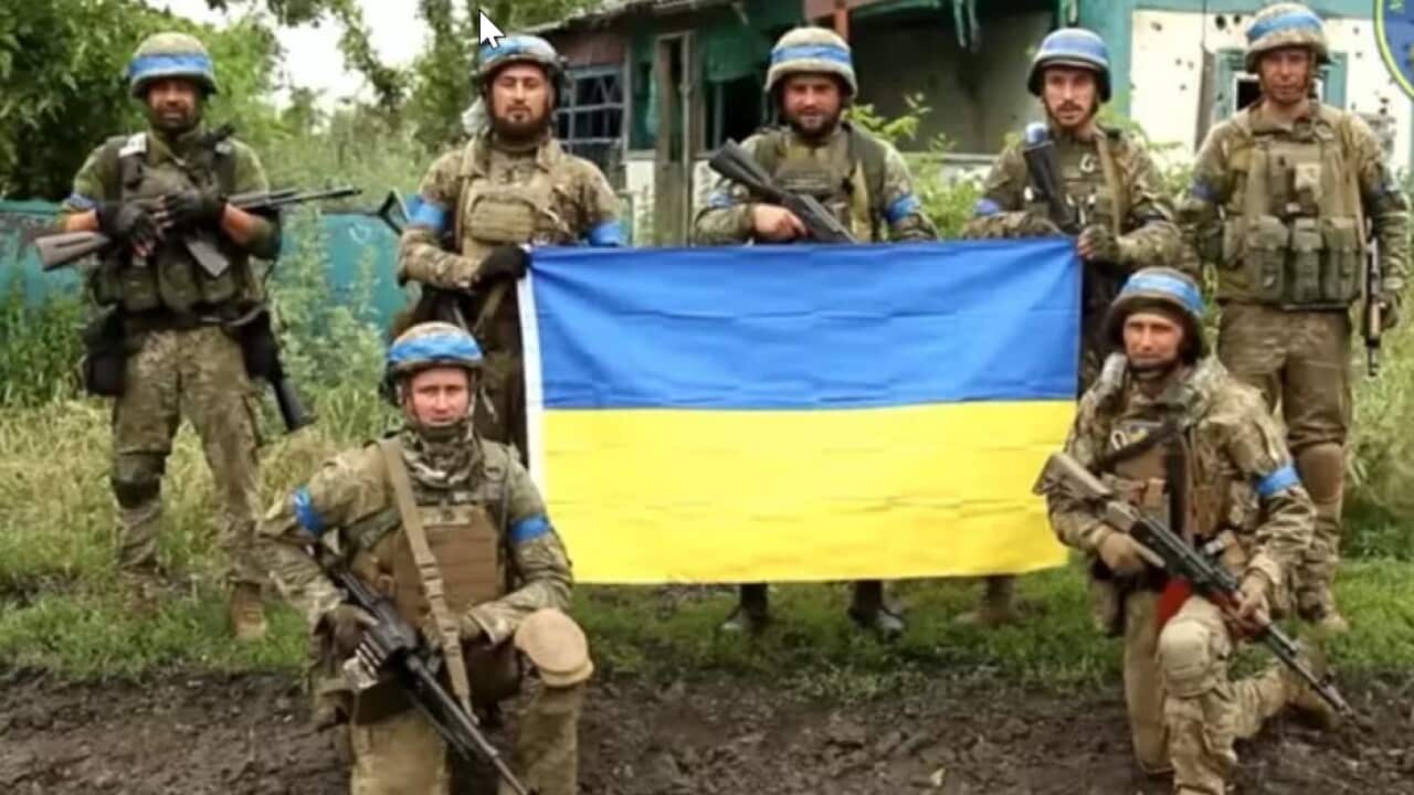 Ukrainian soldiers with Ukrainian flag in front of a house in recaptured area