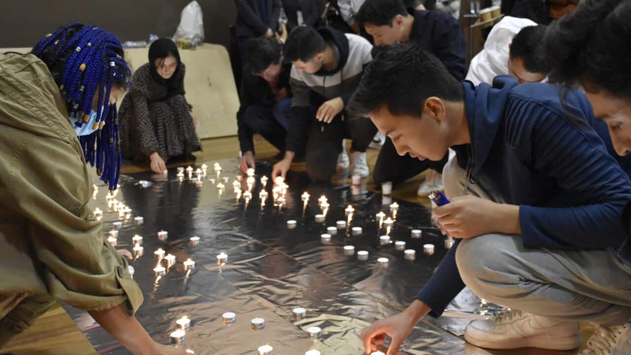 People kneel down to place a lit candle on the floor.