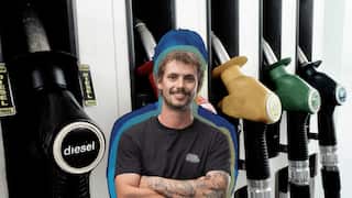 A man smiling and crossing his arms. He is against a background of a petrol pump.