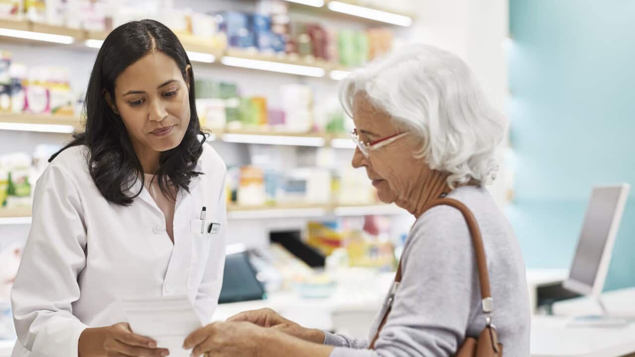 Senior customer showing prescription to female doctor. Cashier is assisting elderly woman at checkout counter. They are standing at pharmacy.