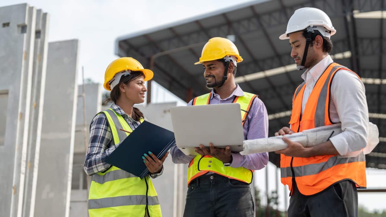 Team of construction engineers wearing vest and helmet safety discussing project at construction site. Group Indian foreman with laptop, paperwork working at factory making precast concrete wall.