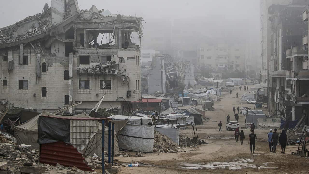 Palestinians walk along a dirt road lined with destroyed buildings and tents