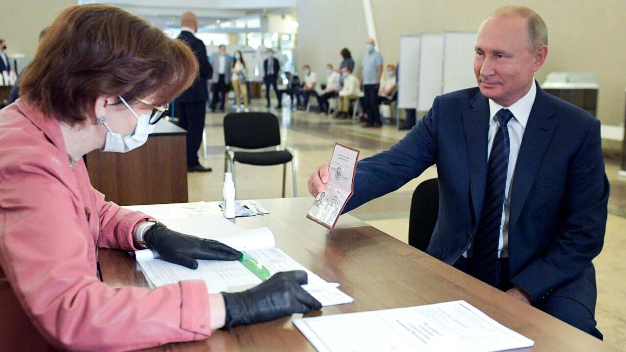 Russian President Vladimir Putin shows his passport to a member of an election commission as he arrives to take part in voting at a polling station in Moscow