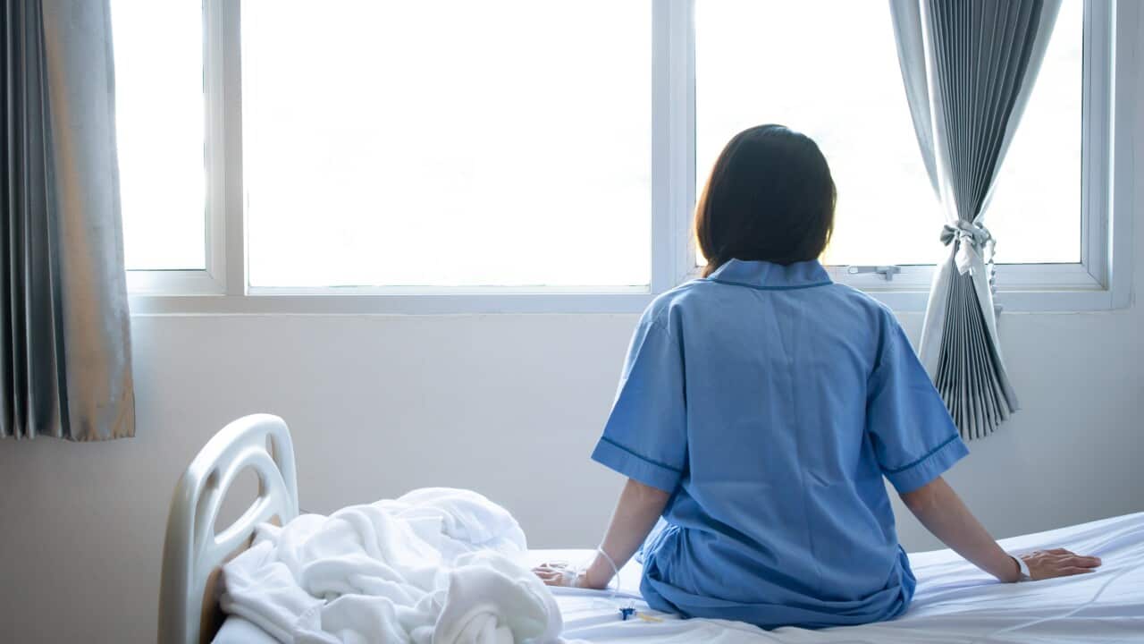 Back view of patient woman sitting on bed in hospital ward, looking away at window