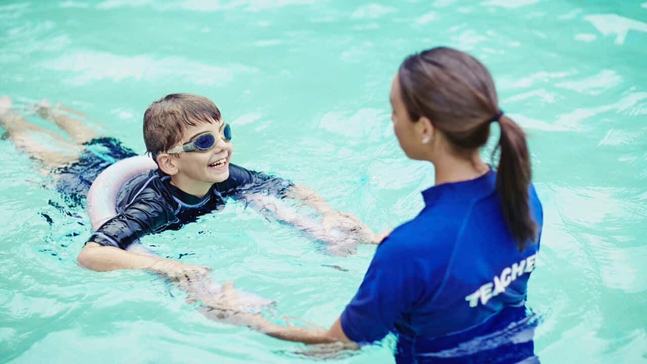 Young boy learning to swim in pool with teacher