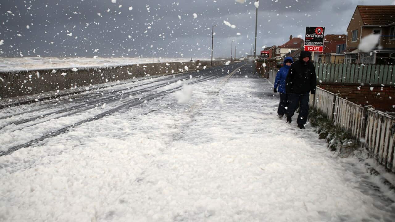 People make their way through foam whipped up by the sea in the UK