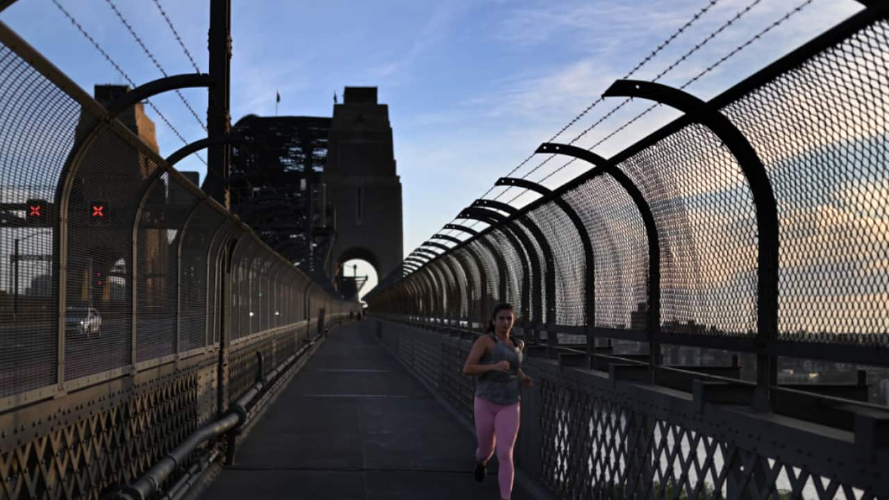 A woman jogs over the Sydney Harbour Bridge at sunrise in Sydney, Thursday, April 2, 2020