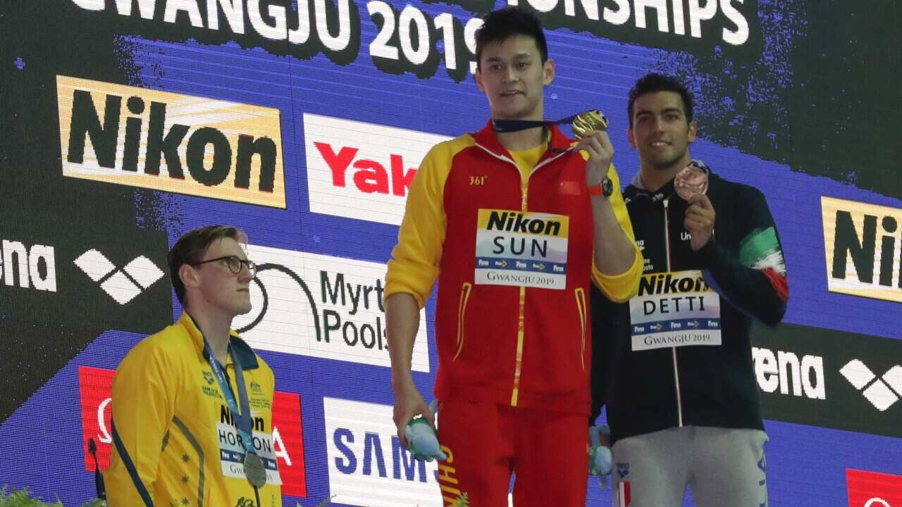 China's Sun Yang, holds up his gold medal as silver medalist Australia's Mack Horton, lstands away from the podium