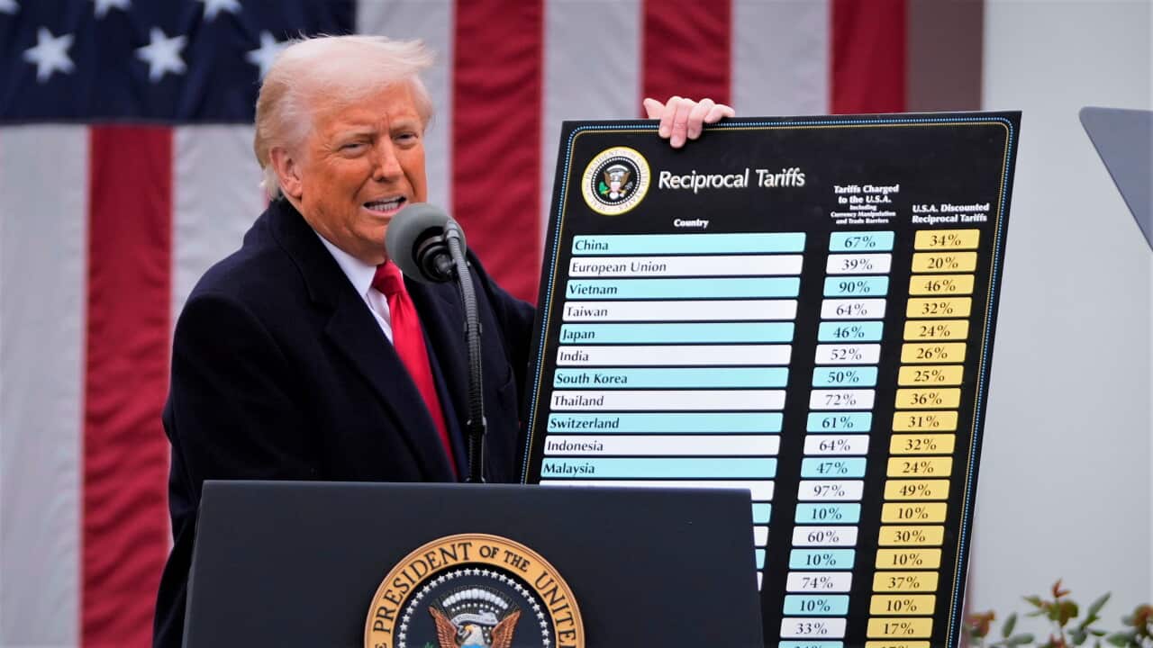 Donald Trump holds a sign reading "reciprocal tariffs" in front of an American flag.