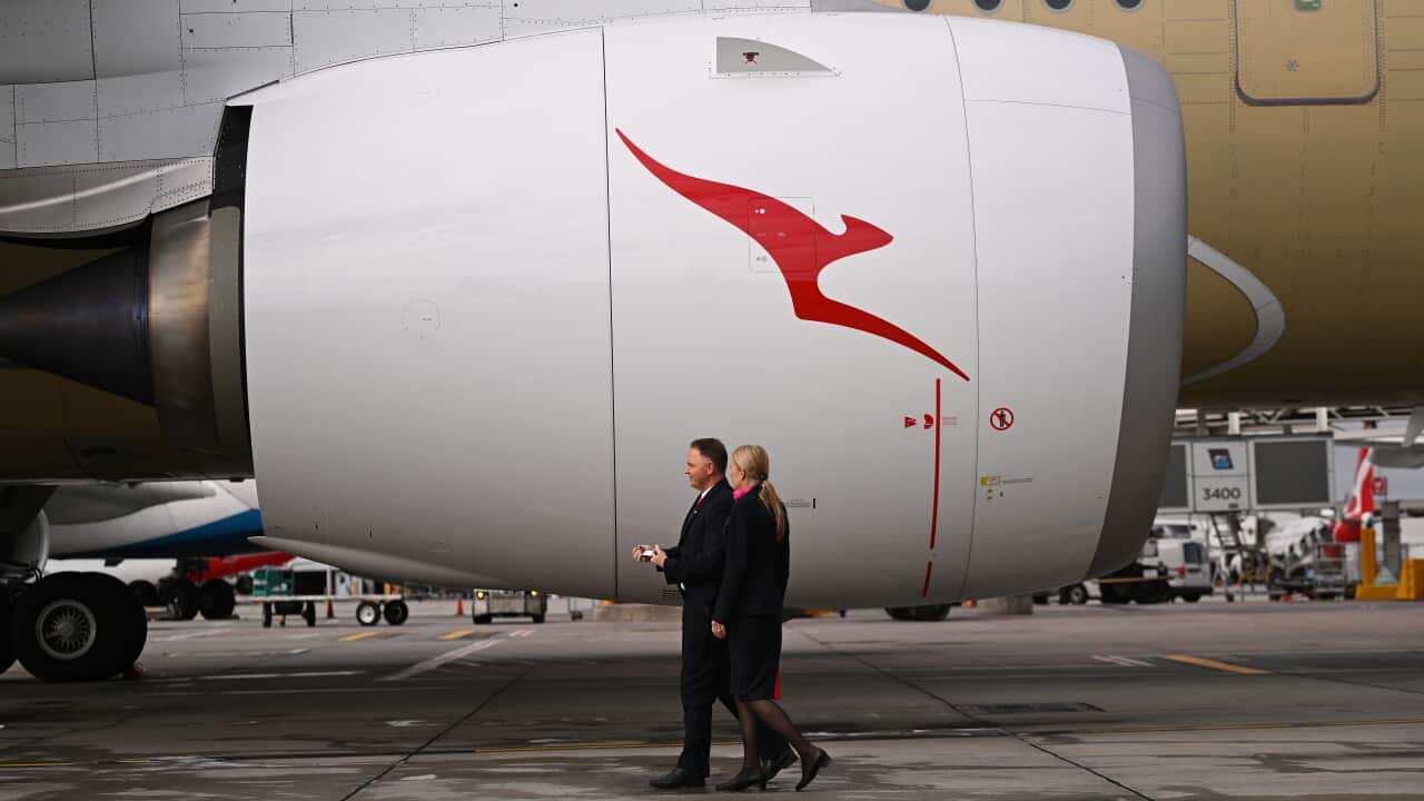 Two people in dark clothing walk past a large aircraft engine with a red kangaroo on it.