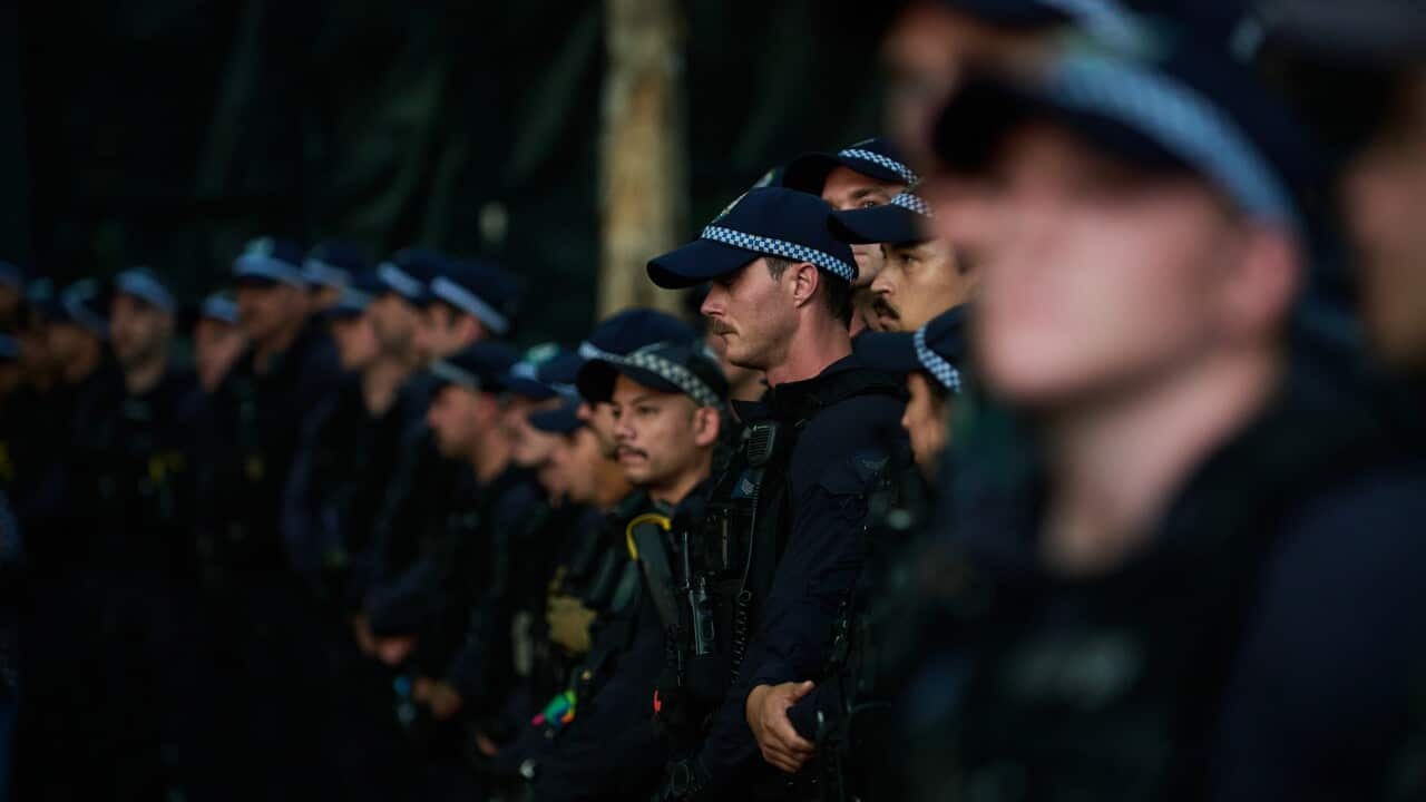 A line of police dressed in dark blue uniforms and hats stare straight ahead.