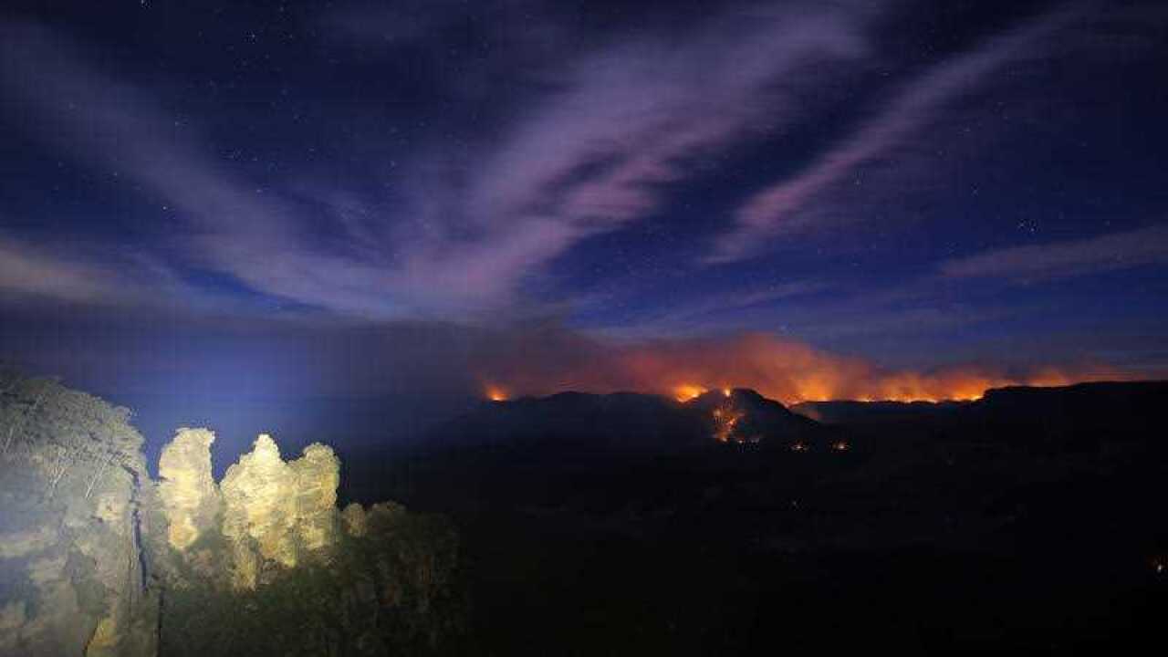 Long exposure photograph shows the Three Sisters rock formation as flames from the Kowmung River fire and the Green Wattle Creek fire are seen from Echo Point.