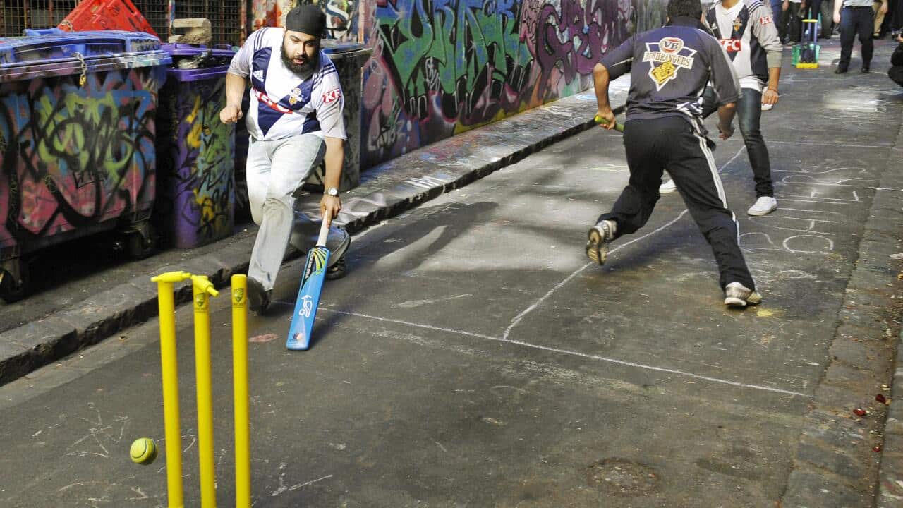 Indian students playing cricket with police officers.