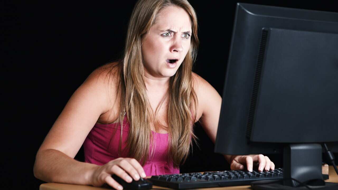 Pretty blonde stares, shocked and disbelieving, at computer monitor