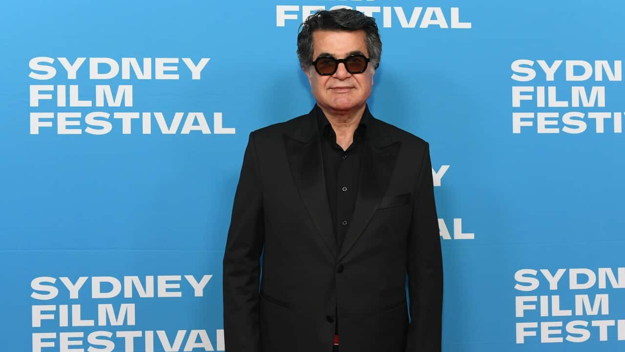 A man in a black suit and sunnies is standing in front of a Sydney Film Festival banner.