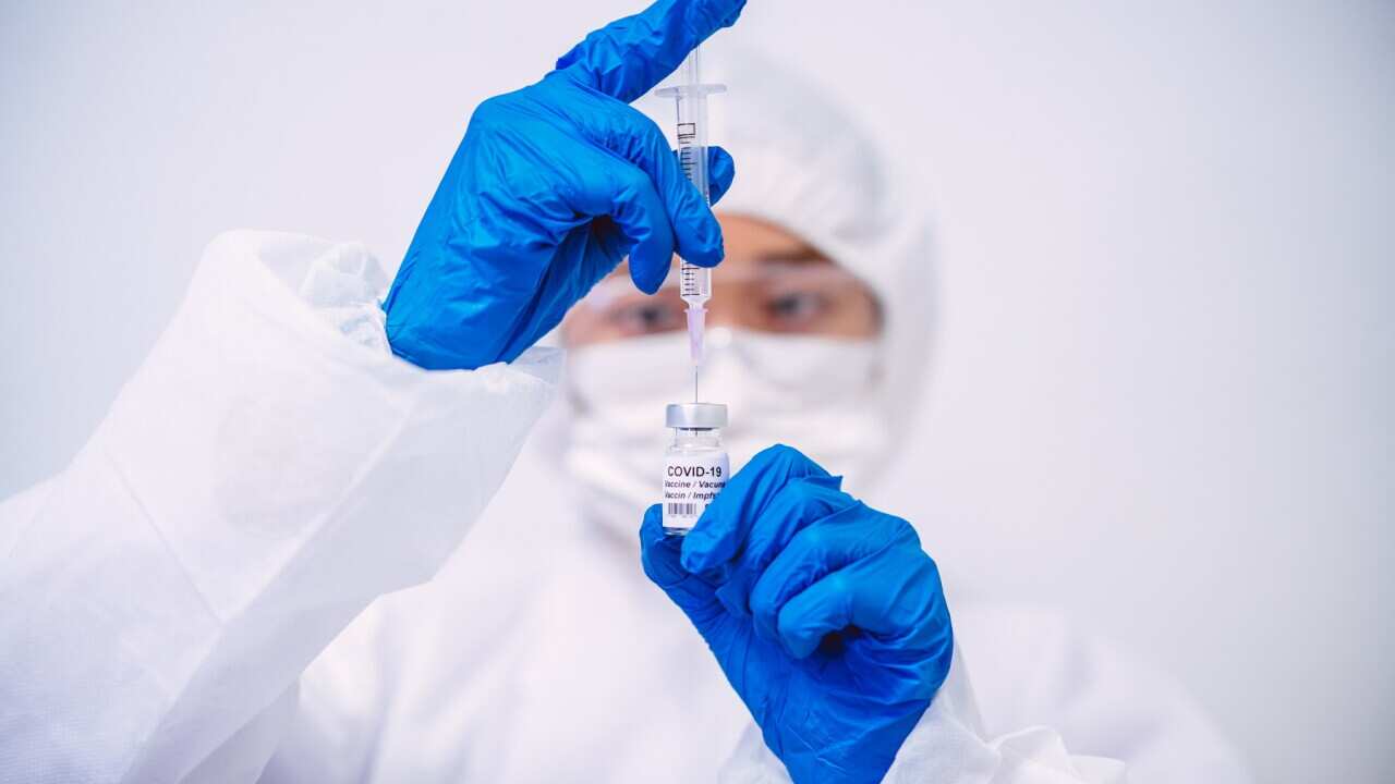 Doctor in protective gloves & workwear filling injection syringe with COVID-19 vaccine