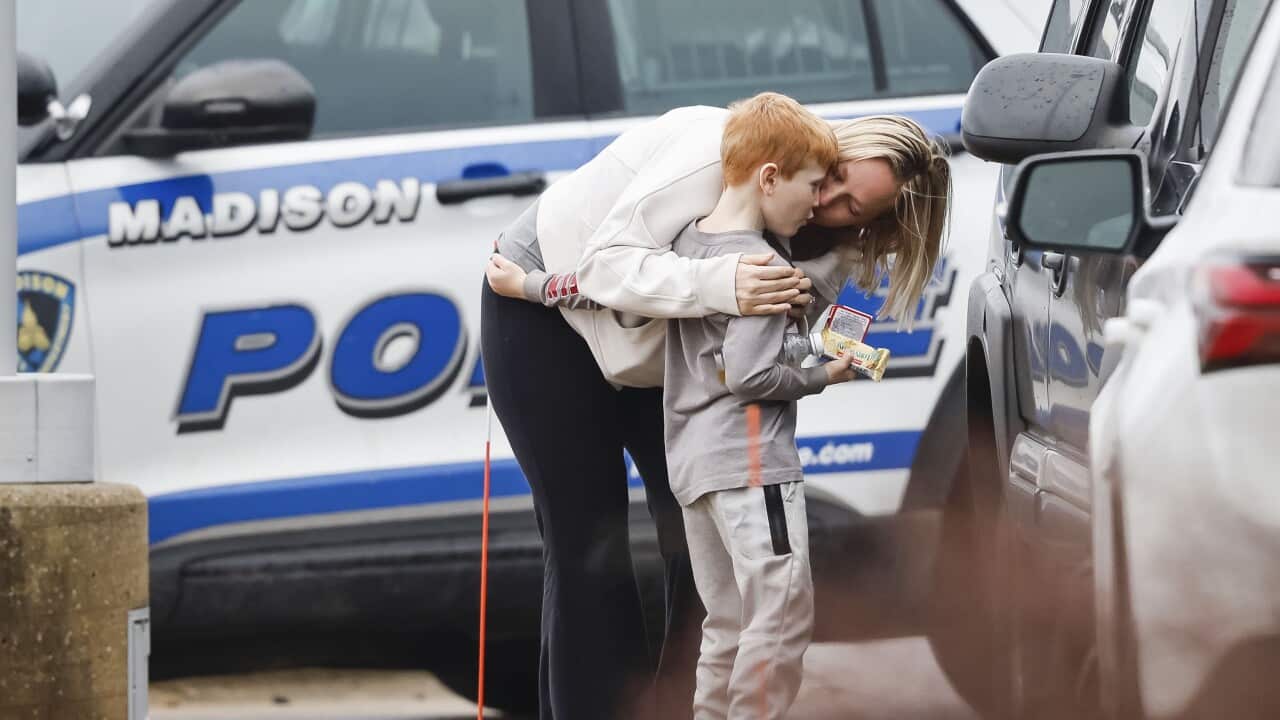 A woman hugging a child with a police vehicle in the background.