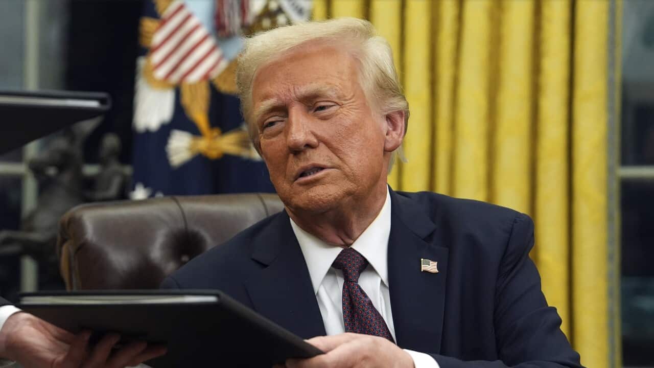 يجلس دونالد ترامب على مكتبه في المكتب البيضاوي، ويتم تسليمه وثيقة.