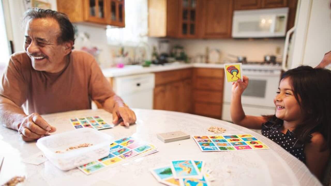A grandfather and his granddaughter laugh as they play a Mexican board game together.